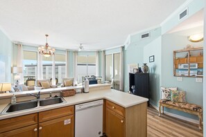 A kitchen with a central island, a dining area with chairs, and a view of a building through large windows. - Magical 3rd-floor condo with pools, telescope for stargazing & pickleball (Santa Rosa Beach)