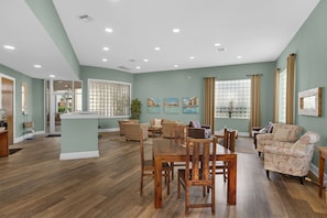 A spacious living room with a dining area, featuring wooden flooring, wicker furniture, and large windows with curtains. - Magical 3rd-floor condo with pools, telescope for stargazing & pickleball (Santa Rosa Beach)