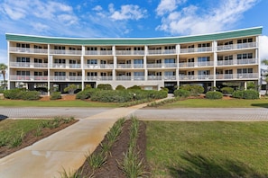 A multi-story hotel with a curved facade, multiple balconies, and a landscaped front yard with pathways and greenery. - Magical 3rd-floor condo with pools, telescope for stargazing & pickleball (Santa Rosa Beach)