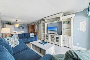 En stue med en blå sofa, et sofabord og et fjernsyn på et hvidt skab.