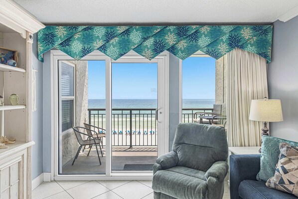 A room with a view of the beach, a grey armchair, a blue sofa, and a patterned throw pillow. - Comfortable waterfront condo with beach chairs - close to dining (Fort Walton Beach)