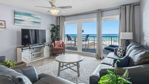 A living room with a TV, sofa, coffee table, and a balcony with a view of the beach. - Comfy beachfront condo with central AC, pool access, ocean view, and washer&dryer (Fort Walton Beach)