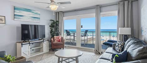 A living room with a TV, sofa, coffee table, and a balcony with a view of the beach.