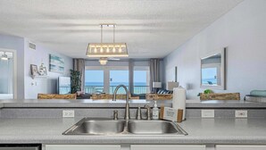 A modern kitchen with a double sink, a chandelier, and a view of the ocean. - Comfy beachfront condo with central AC, pool access, ocean view, and washer&dryer (Fort Walton Beach)