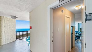 A corridor with a view of the ocean, a door with a security device, and a balcony with a chair.
