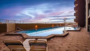 An outdoor swimming pool with lounge chairs, a palm tree, and a sunset view. - Comfortable beachfront condo with beach setup - quick drive to dining! (Fort Walton Beach)