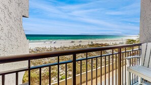 A balcony with a view of a beach, a railing, and a chair. - Comfortable beachfront condo with beach setup - quick drive to dining! (Fort Walton Beach)