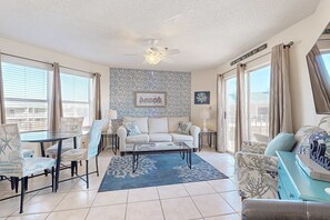 A spacious living room with a glass dining table, comfortable seating, a ceiling fan, and large windows with curtains. - 2nd Floor coastal condo, Steps to the gulf, Quick drive to entertainment (Miramar Beach)