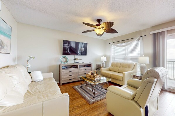 A living room with a ceiling fan, a sofa, a coffee table, and a TV on the wall. - Cozy oceanfront condo with ocean view, pool access, washer&dryer, and central AC (Fort Walton Beach)