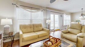 Ein Wohnzimmer mit einem beigen Sofa, einem Glastisch und einem Deckenventilator.