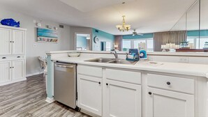 A modern kitchen with white cabinetry, a dishwasher, and a countertop with a sink. - Second floor oceanfront condo with ocean view, balcony, central AC, & pool access (Fort Walton Beach)