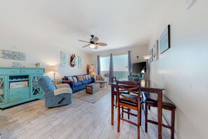 A living room with a blue sofa, a wooden dining table, and a ceiling fan.