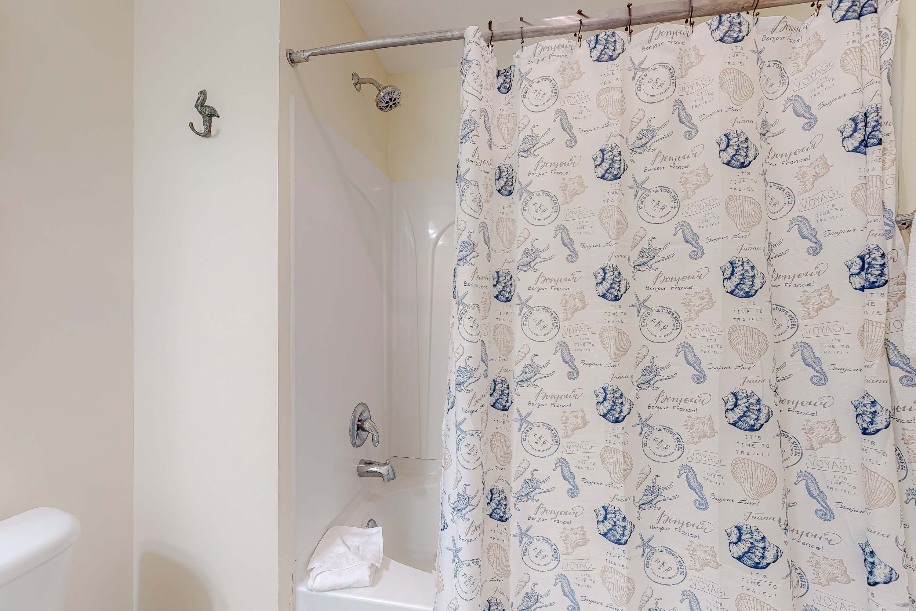 A bathroom with a shower curtain featuring nautical designs and the word "BONJOUR" repeated.