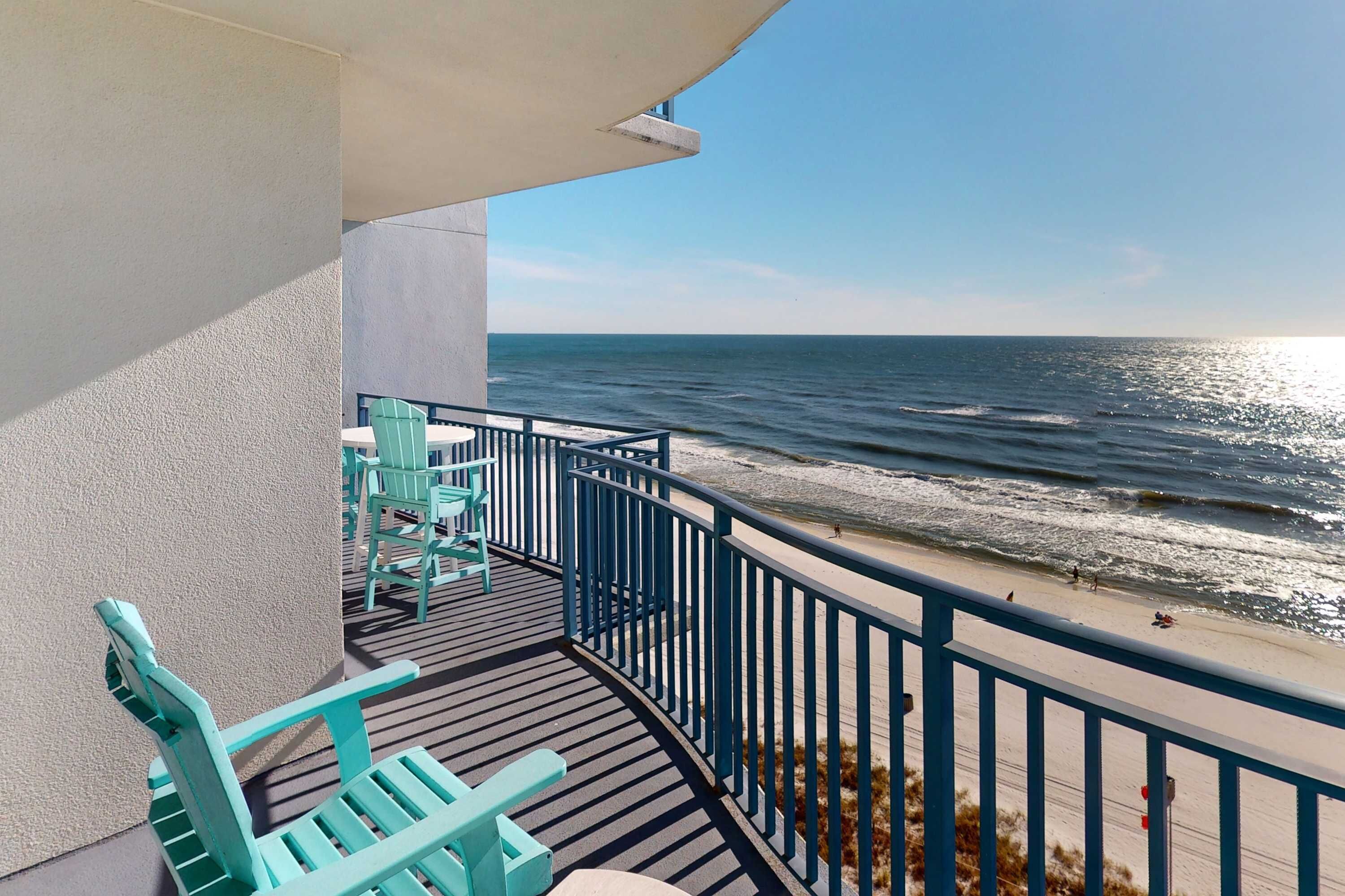 A balcony with a view of the ocean, equipped with turquoise chairs and a table.