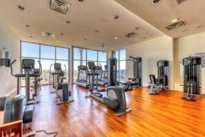 A spacious gym with various cardio and strength training equipment, large windows offering views of the city, and a wooden floor. - Beautiful Gulf-front condo with resort pool & hot tub - right on the beach (Panama City Beach)