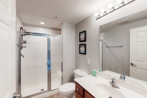 Un baño moderno con ducha de vidrio, inodoro blanco y tocador con un espejo grande.