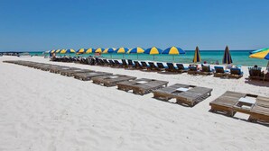 Ein Strand mit mehreren Reihen aus Holzliegen und blauen und gelben Sonnenschirmen.