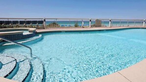 Ein klarer, blauer Pool mit modernem Design, ein Poolbereich mit Liegestühlen und Blick auf den Ozean durch eine Glaswand.