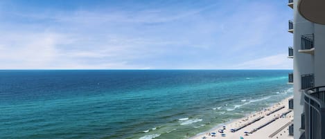 A beach with a clear view of the ocean, a sandy shore, and a building with balconies overlooking the beach.
