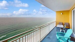 Uma varanda com vista para o oceano, duas cadeiras, uma mesa e uma parede amarela.