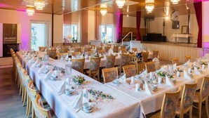 A banquet hall with long tables set for a formal event, equipped with chairs, table settings, and a stage with musical instruments. - Landhotel Wolf-Mertes (Sessenbach)