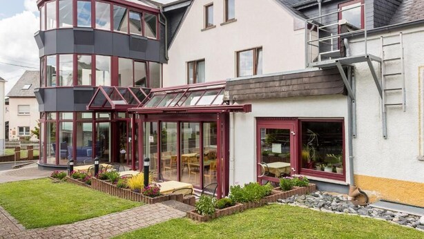 A two-story house with a conservatory, a garden with a patio, and a staircase leading to a second floor. - Landhotel Wolf-Mertes (Sessenbach)