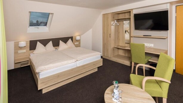 A hotel room with a bed, bedside tables, a TV, a desk with a chair, and a window with a view. - Landhotel Wolf-Mertes (Sessenbach)