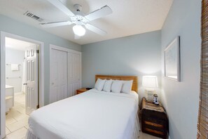 Ein Schlafzimmer mit einem Bett, einem Nachttisch, einer Lampe, einem Deckenventilator und einer Tür zu einem anderen Raum.