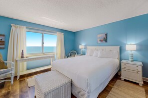 A bedroom with a large bed, a nightstand, a chair, and a window with curtains. - Gorgeous Oceanfront condo with washer/dryer, Gulf-front balcony & pool/hot tub (Perdido Key)
