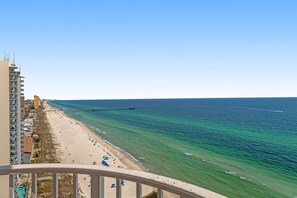 A beach view with a pier extending into the ocean, a sandy beach, and a high-rise building on the left. - Resort style condo w/ shared pools, free WiFi and cable - steps to beach (Panama City Beach)