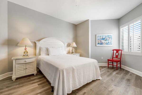 A bedroom with a bed, nightstands, a chair, and a window with blinds. - Resort style condo w/ shared pools, free WiFi and cable - steps to beach (Panama City Beach)
