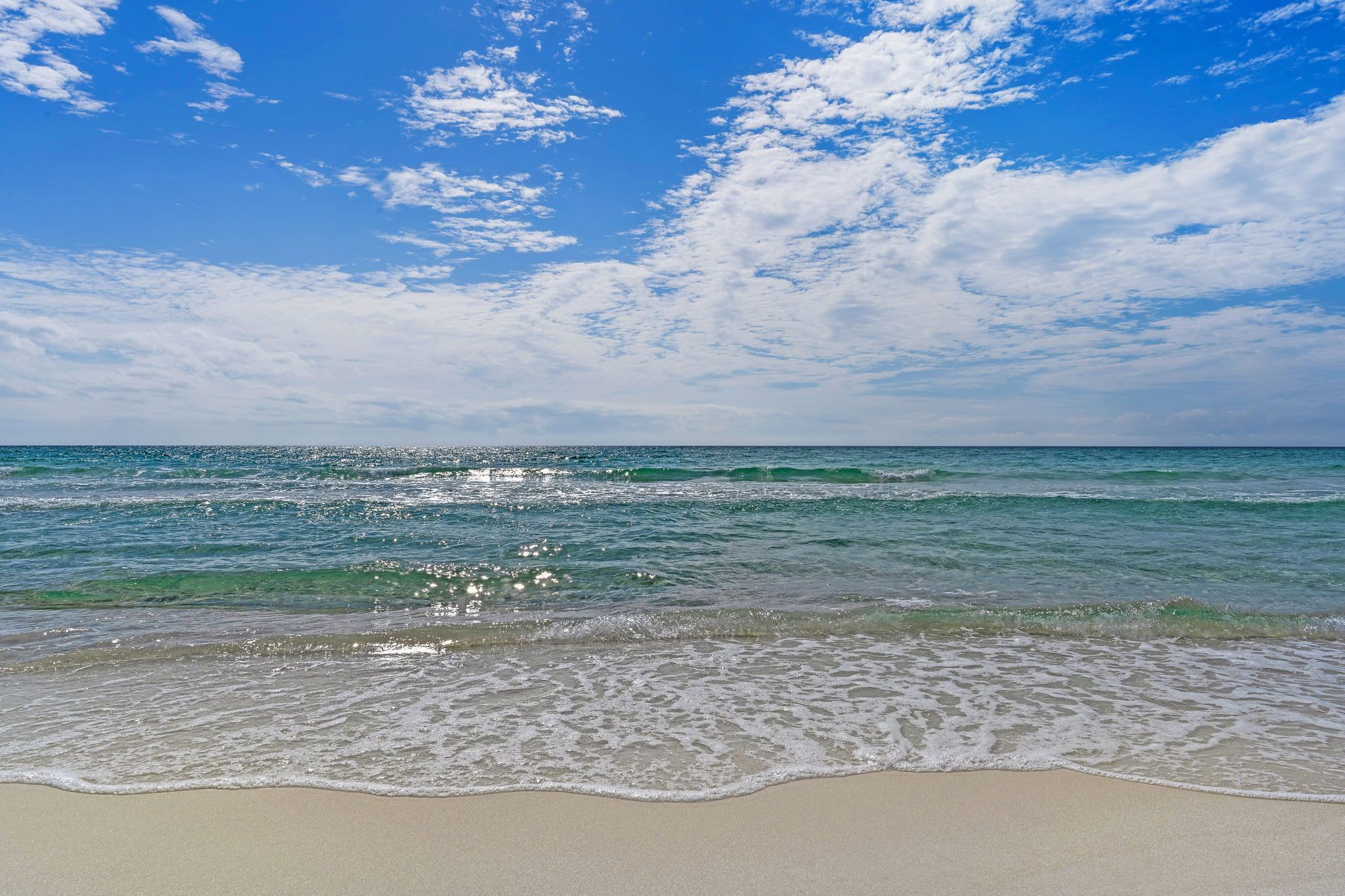 A beach with clear blue water and a sandy shore.