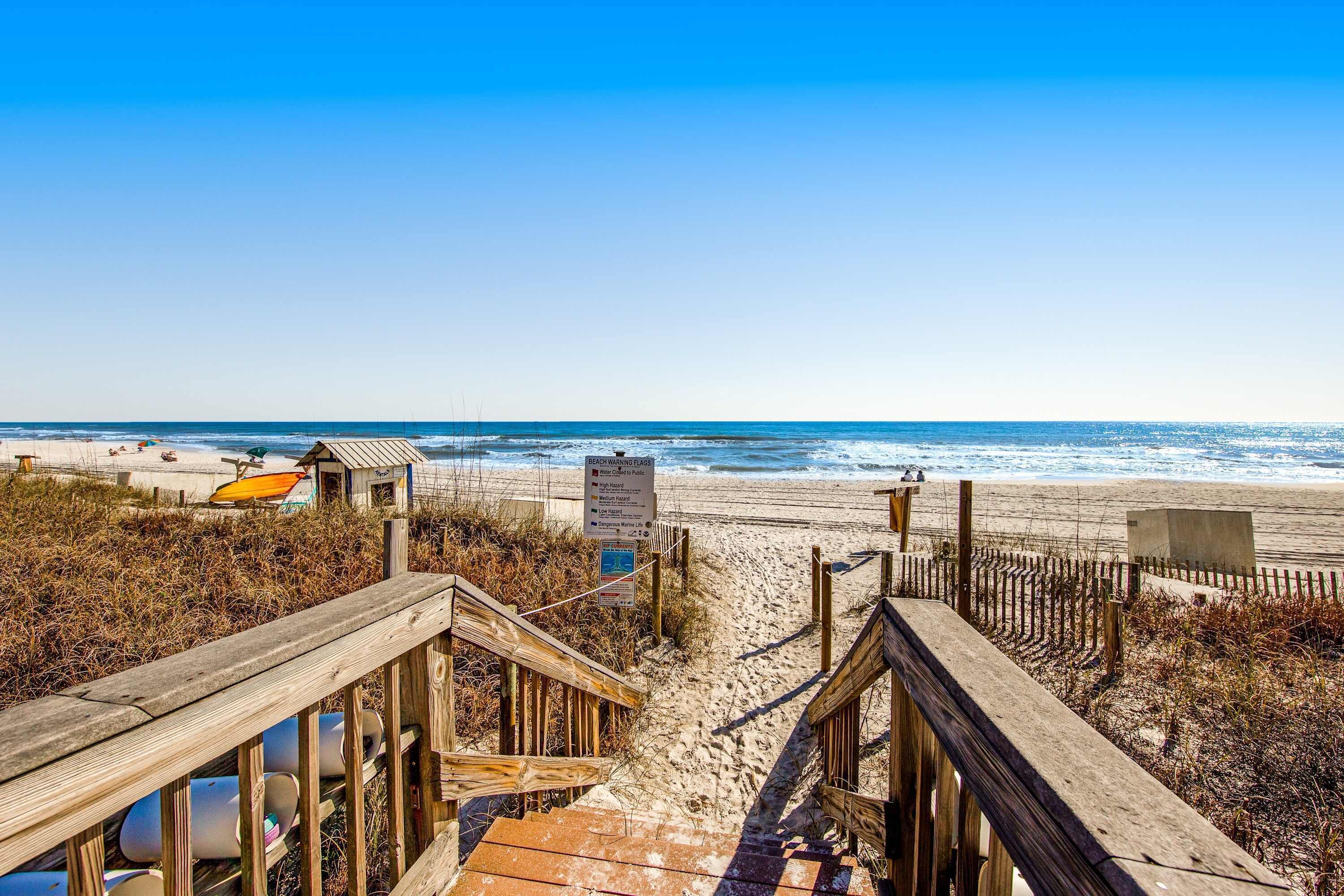 A wooden boardwalk leading to a beach with a lifeguard station and a sign indicating beach rules.