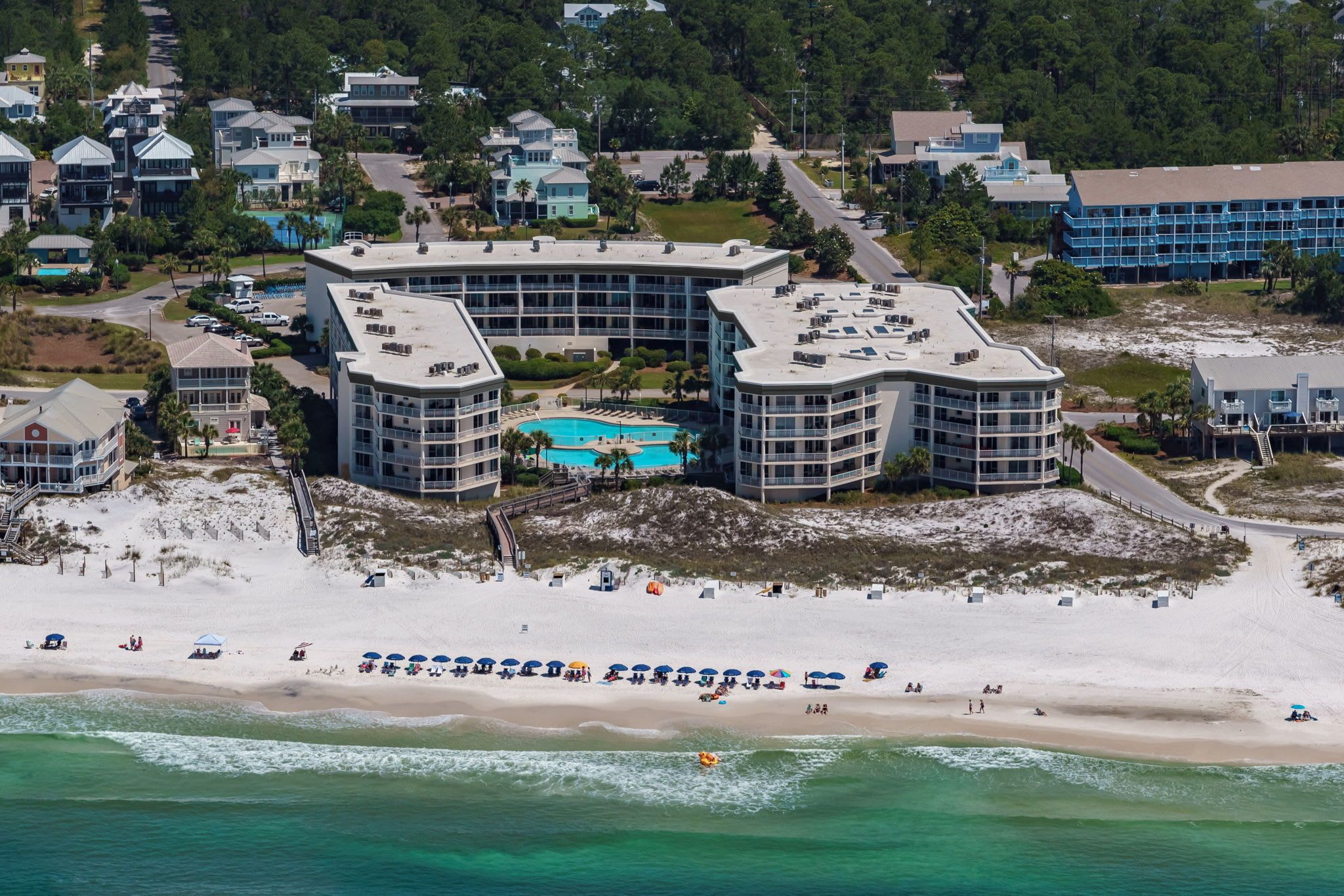 Un hôtel situé en bord de mer, composé de plusieurs bâtiments, doté d’une piscine et bordé d’une plage de sable avec des parasols.