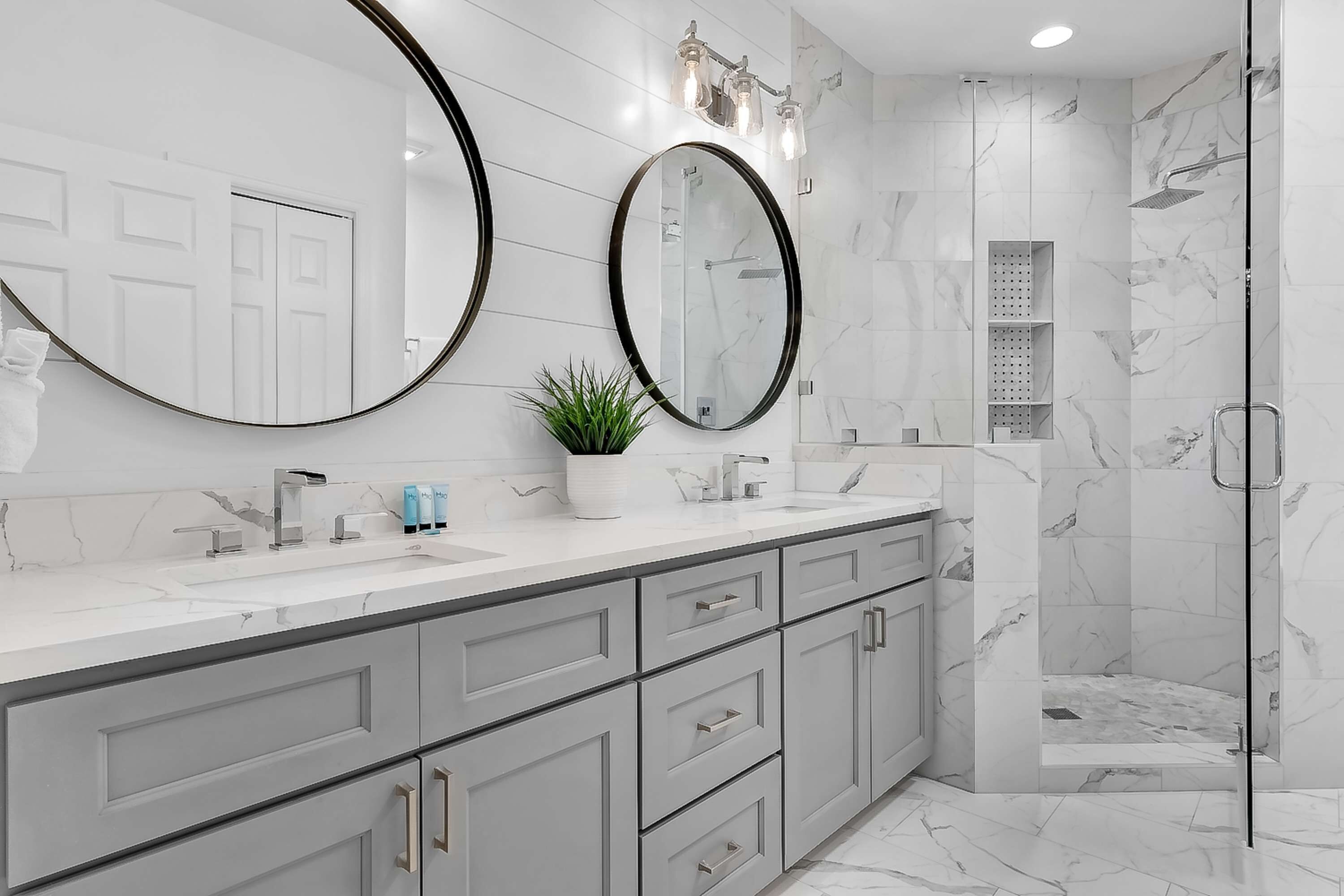 Une salle de bain moderne dotée de deux grands miroirs, d’une cabine de douche et d’un meuble-lavabo avec un plan de travail en marbre.