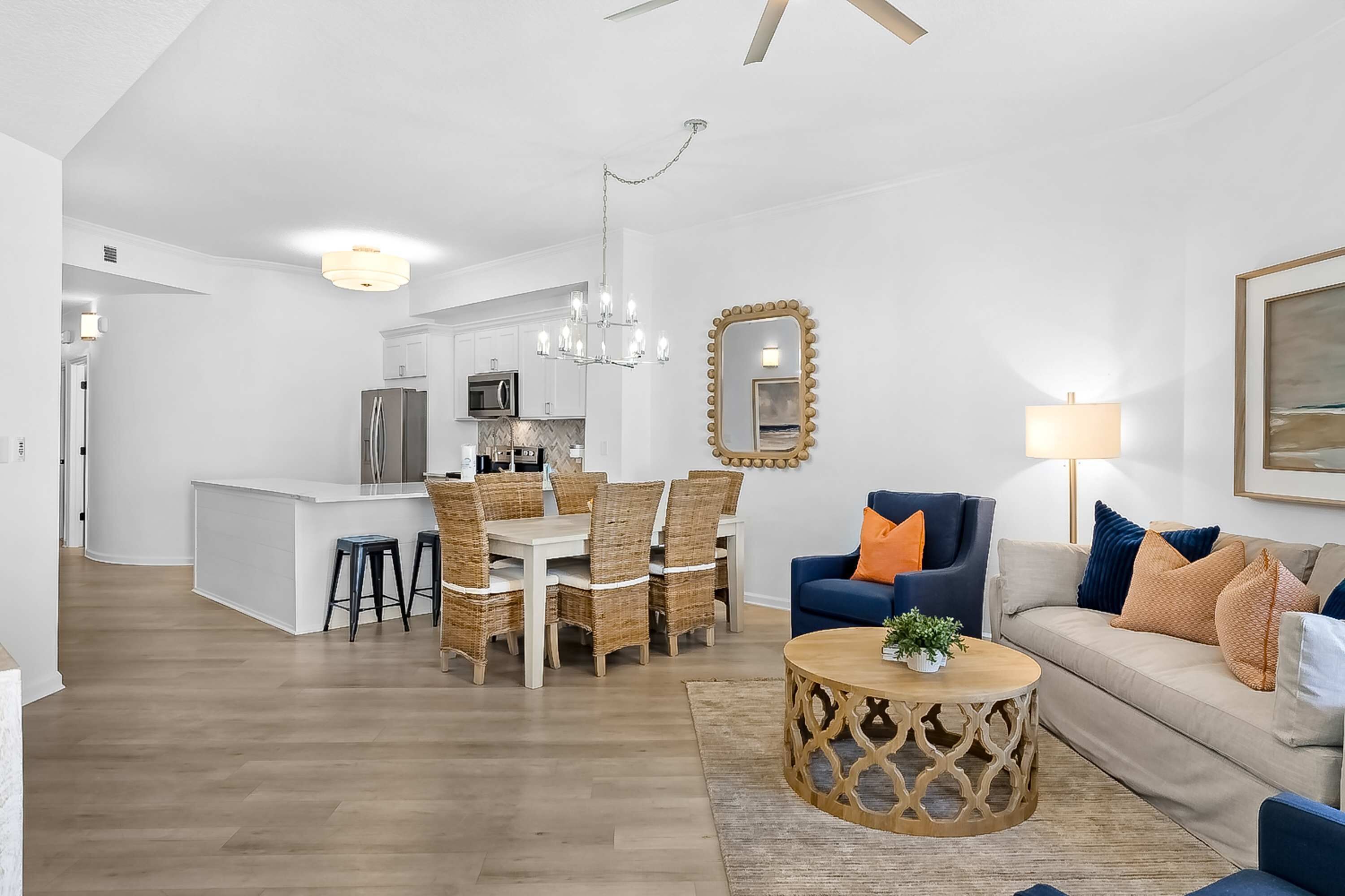 A modern living room with a dining area, a kitchen in the background, and a large mirror on the wall.