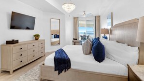 Ein Schlafzimmer mit Bett, Kommode, Fernseher, einer Kristallleuchter und einem Deckenventilator, mit Blick ins Freie.