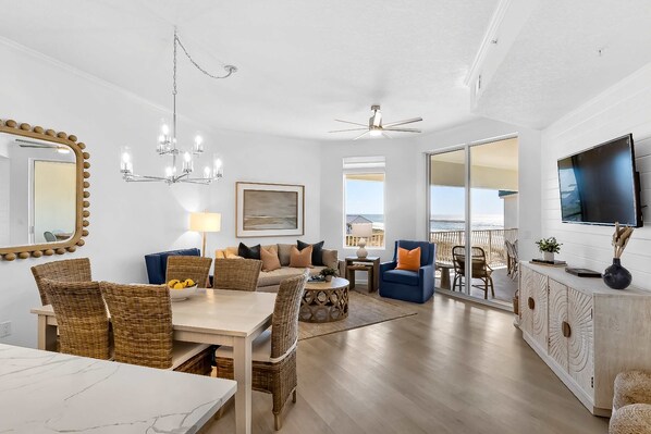 A spacious living area with a dining table, wicker chairs, a sofa with cushions, a coffee table, and a TV on a cabinet. - Dune it Right -Completely Updated with beach access, pool, hot tub, tennis, pickleball & gym (Santa Rosa Beach)