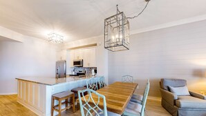 Uma cozinha moderna com armários brancos, uma ilha central e uma área de refeições com mesa de madeira e cadeiras azul-claras.