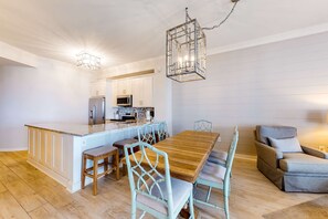 A modern kitchen with white cabinetry, a central island, and a dining area with a wooden table and light blue chairs. - Stunning 4th-floor condo with pool, tennis, pickleball, ocean & beach view (Santa Rosa Beach)