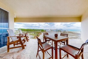 A balcony with wooden furniture, a table, and chairs, overlooking a scenic view of a beach and ocean. - Stunning 4th-floor condo with pool, tennis, pickleball, ocean & beach view (Santa Rosa Beach)
