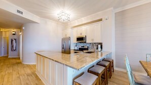 Cozinha moderna com armários brancos, uma ilha central com banquetas, eletrodomésticos de aço inoxidável e uma luminária pendente.