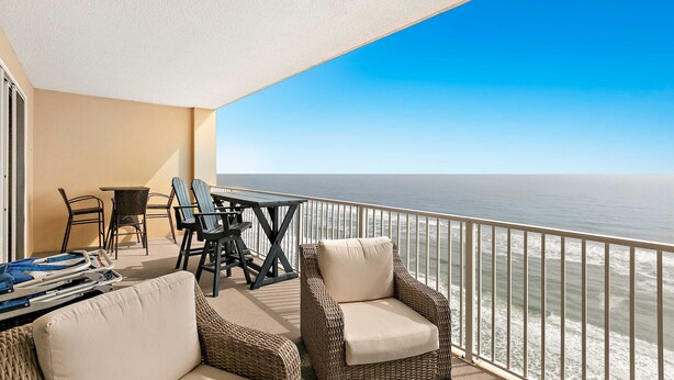 Ein Balkon mit Korbmöbeln, einem Tisch und Blick aufs Meer.