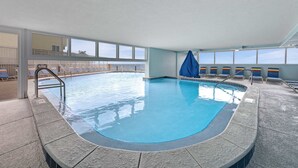 Ein Innenpool mit klarem, blauen Wasser, einer gefliesten Liegefläche und Blick auf den Ozean durch große Fenster.