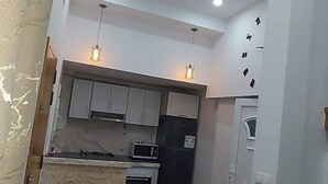 Uma cozinha compacta com armários brancos, micro-ondas, fogão e geladeira. Há luminárias pendentes sobre o balcão.