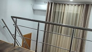 Uma escada com corrimão de metal, porta de madeira e janela com cortinas.