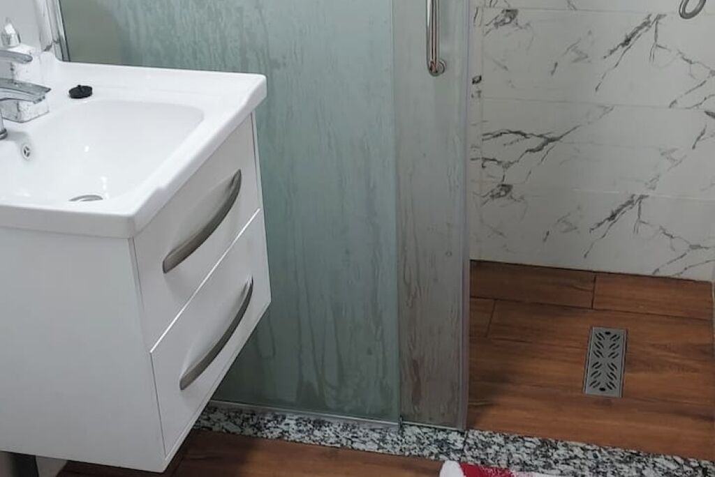 A bathroom with a white sink, a wooden floor, and a marble wall.
