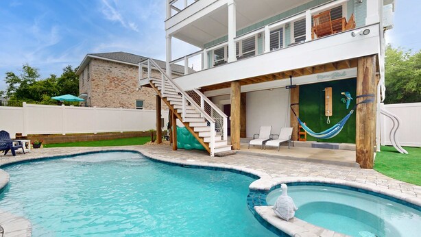 Uma casa de dois andares com piscina, área de estar externa e rede.