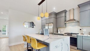 Uma cozinha moderna com armários cinza, uma ilha de mármore e banquetas amarelas.