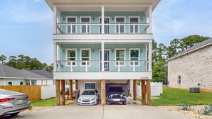 Um edifício de dois andares com varanda no andar superior, uma garagem com dois carros, e um prédio de tijolos à direita.